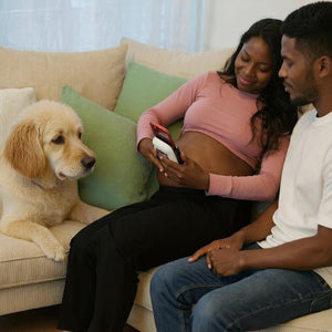 Pregnant woman scanning her pregnant belly on the couch next to her husband and dog