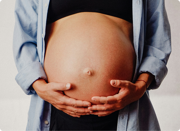 Pregnant woman wearing a light blue shirt holding their pregnant belly.