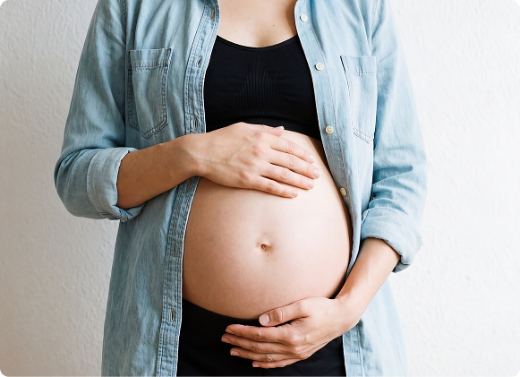 Pregnant woman wearing a light blue denim shirt and black top, holding their pregnant belly.